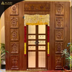 A close-up of the magnificent puja room entrance, showcasing the detailed wooden panels carved with various deities. The traditional flower toran adds a festive and devotional touch.