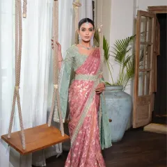 A full-length portrait from a designer shoot featuring a South Indian bridal look. The hair is styled in a neat bun and a long, floral gajara braid, complementing the elegant saree.