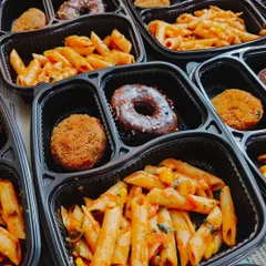 A colorful and balanced meal for a kids' party. These trays are filled with red sauce penne pasta, my signature veg cutlets, and a delicious choco donut for dessert.
