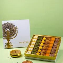 An open box of assorted Indian sweets for Meethi India. The composition includes the branded box lid and almonds to showcase the product's context and quality.