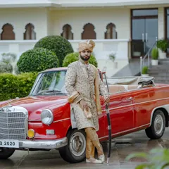 A portrait of modern royalty. The groom stands with confidence beside a classic red vintage Mercedes, his sherwani and turban perfectly complementing the regal setting. This shot blends classic style with a hint of cinematic flair.