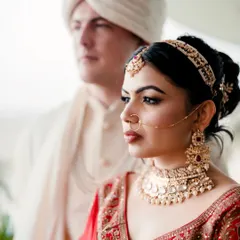 A close-up, artistic portrait focusing on the bride's beauty, with the groom slightly out of focus in the background. This composition creates depth and a sense of cinematic storytelling.
