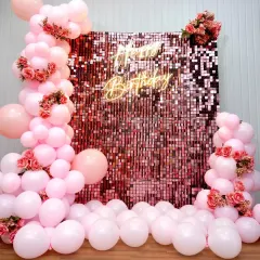 A gorgeous pink sequin wall for a birthday celebration. The shimmering backdrop is framed by soft pink balloons and accented with artificial roses, creating a romantic and glamorous photo spot.