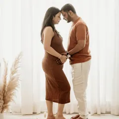 A full-length portrait showcasing a tender forehead-to-forehead pose. This silhouette against the bright window highlights the couple's bond and the beautiful baby bump.