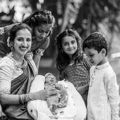 A mother and the older children gather around to admire the family's newest member. This black and white photograph highlights the sweet curiosity and affection of siblings during a naming ceremony.