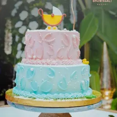 A detailed look at the two-tiered baby shower cake. It features soft pink and blue pastel frosting with delicate textures and an adorable baby carriage topper.