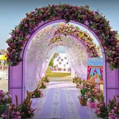 A stunning purple-themed entrance arch, heavily decorated with flowers and draped with sheer fabric, leading into an outdoor event space.
