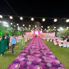 A long view of an outdoor reception aisle. The purple patterned carpet leads guests through the seating area directly to the main stage, creating a grand sense of arrival.