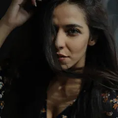 A dramatic, moody portrait where the model's face is partially obscured by her hair and shadows. This close-up shot focuses on her intense gaze, demonstrating a more artistic and emotive approach to fashion photography.