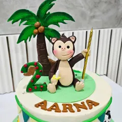 A cheerful jungle-themed cake for a second birthday. The topper features a playful monkey holding a banana, a custom nameplate, and a number '2' candle, all crafted from fondant.