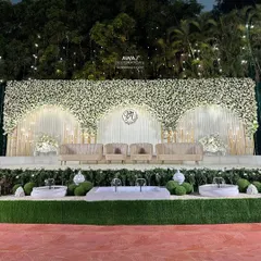 A vision of pure elegance, this outdoor stage features a breathtaking arch of white flowers against a clean, white-draped backdrop, complemented by plush, modern seating.