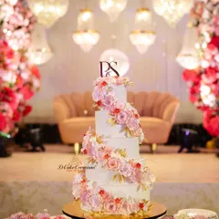 A classic love story calls for a timelessly romantic cake. This five-tier wedding cake features a cascading spiral of handmade sugar flowers in soft pinks and whites, accented with delicate gold leaves for a touch of luxury.