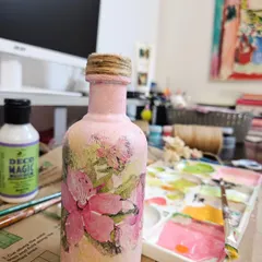 Here is a look at one of my one-of-a-kind decoupage pieces. I love transforming simple glass bottles into unique home decor items. This one features a soft pink texture and delicate floral motifs, perfect for a boho chic space.