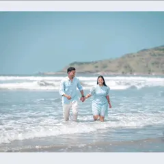 A happy couple holds hands while walking through the gentle waves of the sea, a perfect example of a relaxed and natural beach pre-wedding shoot.