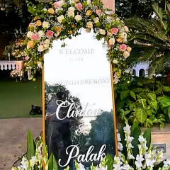 A mirrored welcome sign for a wedding, elegantly scripted with the couple's names and surrounded by pastel roses.