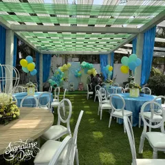 The overall view of the baby shower, with blue and green draping creating a tented effect. Tables are dressed in blue with white chairs, creating a fresh and celebratory atmosphere.
