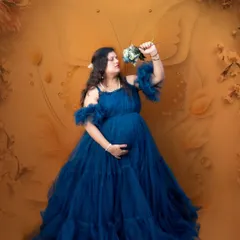 A mother-to-be in a flowing blue gown, holding a bouquet against a warm, butterfly-themed backdrop. A beautiful and artistic way to capture the pregnancy glow.