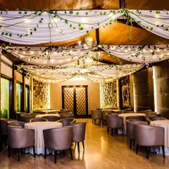 A rustic and elegant indoor venue decoration. We draped the ceiling with white fabric and intertwined fairy lights and green vines, creating a warm and magical ambiance for a dinner or reception.