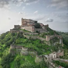 A dramatic, wide-angle shot of Kumbhalgarh Fort under a cloudy sky. This perspective showcases the fort's dominance over the surrounding Aravalli hills and captures a sense of its timeless, enduring presence.