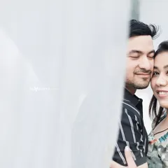 A soft and dreamy close-up of a couple, partially obscured by a white curtain. This artistic shot focuses on their serene and happy expressions.