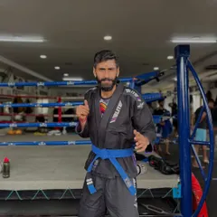 I stand in my Brazilian Jiu-Jitsu blue belt Gi in front of the ring. We are a complete combat sports gym, with strong programs in both striking and grappling.