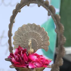 A traditional brass peacock diya filled with fresh rose petals serves as a beautiful and symbolic welcome element. This small detail adds a touch of grace and auspiciousness to the entrance of any spiritual gathering or wedding.
