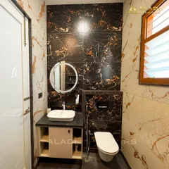 A luxurious bathroom featuring walls tiled with dramatic black and gold marble. A simple round mirror and white vessel sink provide a beautiful contrast.