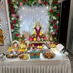 This is a complete view of our popular rose arch decoration in a client's home. The frame of red, pink, and white roses with green leaves, paired with a simple curtain and fairy lights, creates a full and festive space for Bappa and all the puja offerings.