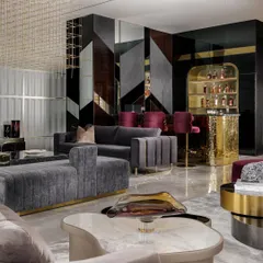 This perspective highlights the custom bar unit, featuring an arched, illuminated display for spirits and a hammered brass front. The design seamlessly connects the bar with the main lounge, which includes plush grey sofas and a unique marble-topped coffee table.