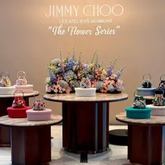 A multi-level product display showcasing Jimmy Choo's new collection. Each handbag is presented on its own table, surrounding a central, grand floral arrangement that unifies the entire presentation.