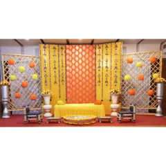 A complete and symmetrical Haldi stage with a bright yellow and orange theme. The setup includes low seating, floral pomanders, and decorative vases on a red carpet.