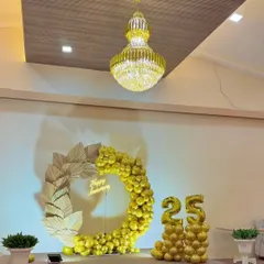A luxurious all-gold theme for a 25th anniversary. This decor features a golden balloon arch with dried palm leaves, a "Happy Anniversary" sign, and large foil "25" balloons.