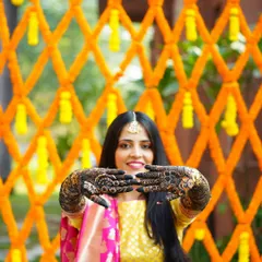 The bride proudly showing off her intricate Mehendi design. The vibrant orange marigold backdrop makes the deep color of the henna pop.