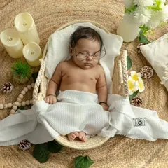 A peaceful newborn in a simple, boho-inspired setup. The natural textures, soft white wrap, and gentle lighting create a serene and timeless portrait that focuses on the baby's delicate features.