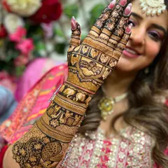 A happy bride showcasing her beautiful back-of-hand mehndi. The deep, dark stain of the henna looks stunning against her skin and complements her bridal attire perfectly.