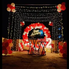 A beautiful terrace setup for a second anniversary. The decoration features a red and white balloon circle, a "Happy Anniversary" neon sign, and a canopy of fairy lights creating a romantic ambiance.