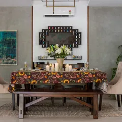 This dining space blends contemporary minimalism with rustic charm. A solid wood bench is paired with upholstered chairs around a table set with a vibrant floral cloth, all against a backdrop of textured grey walls and modern art.
