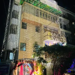 A beautifully decorated wedding house at night. The building is draped in fairy lights, and the entrance gate is adorned with pink drapes and floral arrangements.