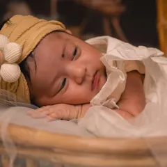 A close-up portrait of a sleeping newborn, peaceful and serene. For these styled infant photos, I use soft fabrics and simple accessories like this floral headband to keep the focus on the baby's delicate features.