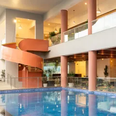 The Sona Vistaas Clubhouse in Bangalore, where a bold, terracotta-red spiral staircase serves as the social and architectural heart of the space. The open, multi-level design encourages interaction, with the swimming pool reflecting the structure and creating a dynamic interplay of light and form.