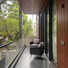 This balcony is designed as a private outdoor retreat. The space features comfortable seating, a wood-paneled soffit that adds warmth, and a glass railing that ensures an unobstructed view of the surrounding greenery.
