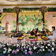 A wide view of a traditional naming ceremony in progress. The decor features a hand-painted backdrop with tropical motifs and an abundance of fresh flowers on the floor, creating a sacred space.