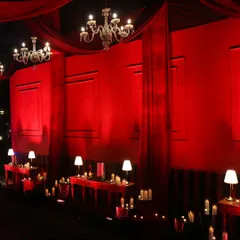 A long passageway draped in rich red fabric and lit by elegant chandeliers and table lamps, creating a grand and theatrical entrance.