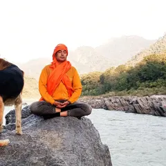 I find my peace in nature, and I guide you to find yours. Here, I am in meditation by the river in Rishikesh, a practice of connecting with the self that I share in every retreat.