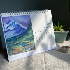 The February page of my art calendar, showcasing a dramatic acrylic painting of blue and purple mountains. Each month offers a new piece of art to brighten your desk.