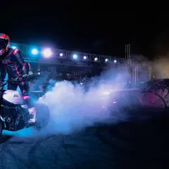 We create a spectacle of light, sound, and skill. A rider performs a burnout on a custom motorcycle, with vibrant blue smoke filling the arena under the glow of professional stage lighting, captivating the crowd.