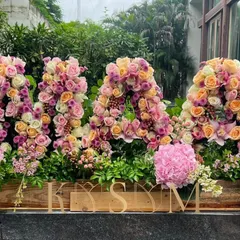 For a milestone birthday, I created this 'MAA' arrangement with big love. Using a palette of pinks and peaches, this floral sculpture combines roses, hydrangeas, and lilies in a custom wooden box for an immense display of joy.