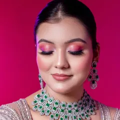 A detailed close-up shot designed to highlight technical makeup skill. The model's eyes are closed to fully display the vibrant pink and magenta eyeshadow blend. This image also showcases the stunning emerald and diamond necklace set provided as part of our styling service.