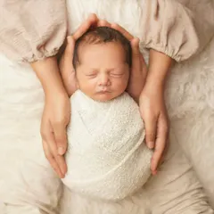 A mother's hands gently cradle her swaddled newborn. This pose emphasizes the feeling of safety and love, creating a powerful memory of how small your baby once was.