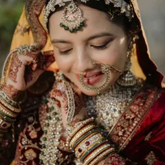 A close-up capturing the bride's gentle smile and the intricate details of her nath (nose ring) and maang tikka. These shots celebrate the fine artistry of bridal adornment.